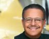 AutoGyro A smiling man with glasses, short dark hair, and a mustache is shown in the foreground. The background features a blurred yellow and gray industrial setting.