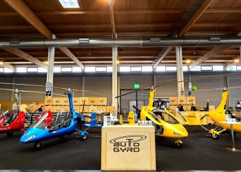 AutoGyro booth at the AERO 2024. In the front is a front desc with an AutoGyro logo and four gyroplanes in red, blue and yellow colour.