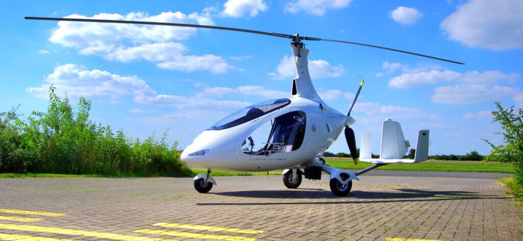 AutoGyro A sleek, white gyroplane with a streamlined design stands on a paved surface under a bright blue sky with scattered clouds, symbolizing a certifications achievement